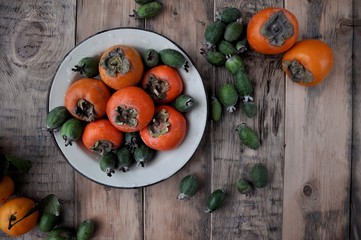 On the table in a plate or box a fresh persimmon, feijoa and citrus mandarins