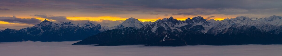 Panorama of austrian mountains during sunset with a layer of clouds below.