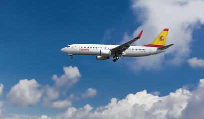 Fototapeta na wymiar Commercial airplane with Spanish flag on the tail and fuselage landing or taking off from the airport with blue cloudy sky in the background