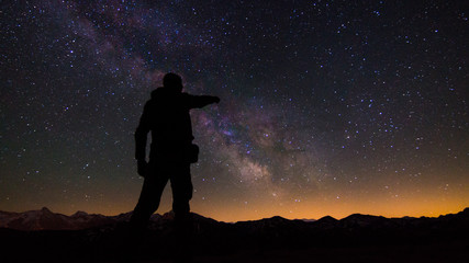Person pointing at the milky way in a mountainous landscape. - obrazy, fototapety, plakaty