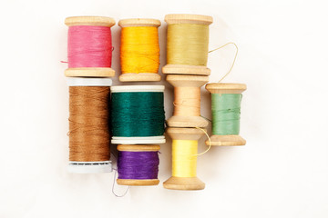 Different colour thread on wooden spools on a white background