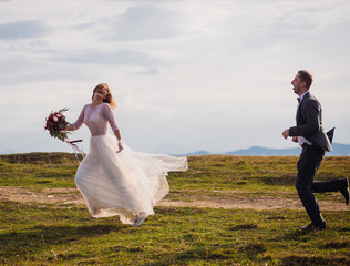 Bride and groom run on the hill before beautiful mountain landscape