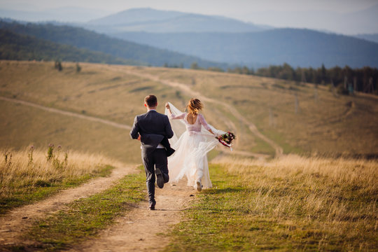 Bride and groom run on the hill before beautiful mountain landscape