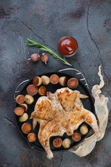 Above view of roasted chicken tabaka with fried cherry potatoes and sauce on a cracked asphalt background