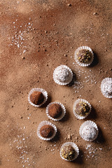 Variety of homemade dark chocolate truffles with cocoa powder, coconut, walnuts over cocoa powder as background. Top view, copy space.
