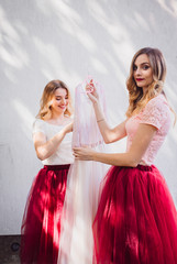 Fototapeta na wymiar Bridesmaids in pink dresses get ready bride's gown
