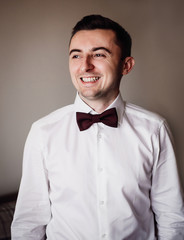 Groom puts on his shirt red bow tie standing in the room