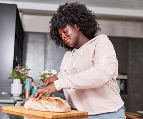 Fototapeta na wymiar Kurvige afrikanische Frau schneidet Brot in Küche