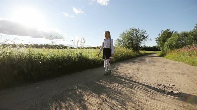 Small girl in white shirt and black skirt is going to school by the sandy road.