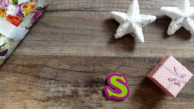 A man's hand forms the word xmas on a wooden table with Christmas decorations