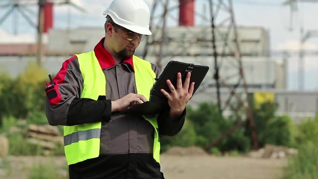 Power engineering specialist with personal computer at heat electric power station. Worker in hard hat at heat electric power station, engineering supervision. Factory worker with tablet pc