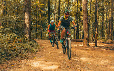Obraz premium Two mountain bikers riding bike in the forest on dirt road.