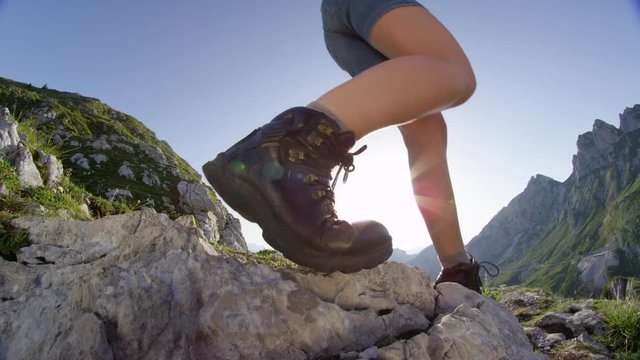 SLOW MOTION CLOSE UP: Unrecognizable female hiker walking down a green mountainside on sunny summer day. Young woman in brown hiking boots descending from a mountain summit on fresh spring morning.