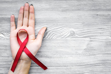 Hand hold red ribbon for HIV, AIDS, substance-abuse and anorexia awareness on grey wooden background top view copyspace