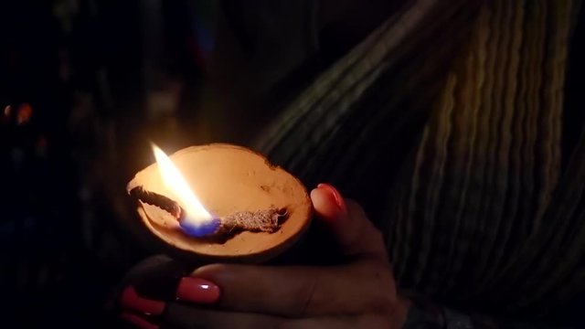 womans hands are holding lighted ancient clay oil lamp in dark church