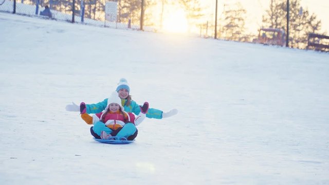 Family rides a sledding down on snow disk in sunny day against sunset