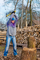 A man, a woodcutter with a yellow ax, chop wood for a fire on the background of a pile of firewood.
