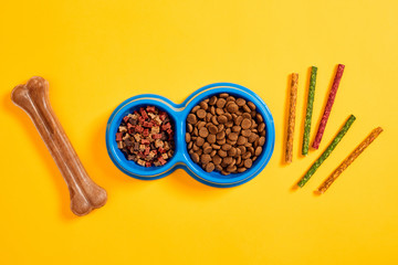 Dog food in blue bowl and accessories on yellow background