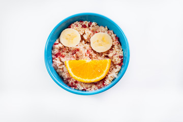 Oat porridge in a bowl, with orange and banana. Smile. On a white background.