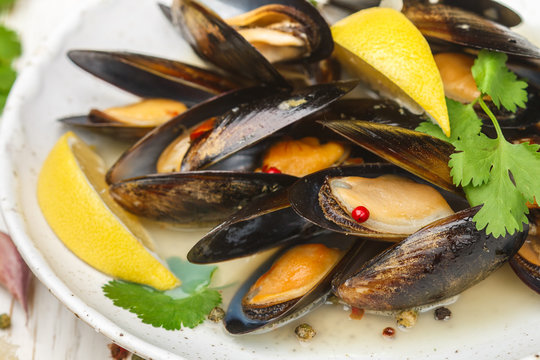 Delicious mussels in white wine with lemon, garlic, herbs and spices close up . Cilantro and pepper. Seafood. Clams in the shells. Snack for gourmets. Selective focus