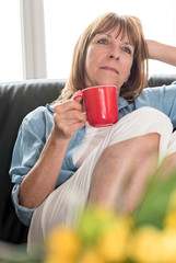 Pensive mature woman sitting on sofa