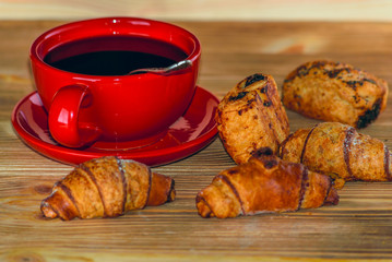 croissants on a wooden background on a red plate and coffee mug