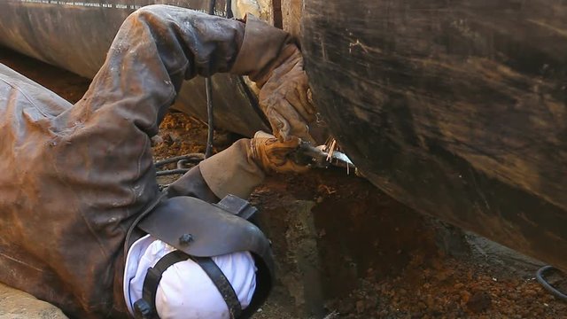 Welder is in trench working hard, arc welding pipeline.
