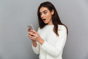 Close-up photo of surprised brunette girl holding and looking at mobile phone