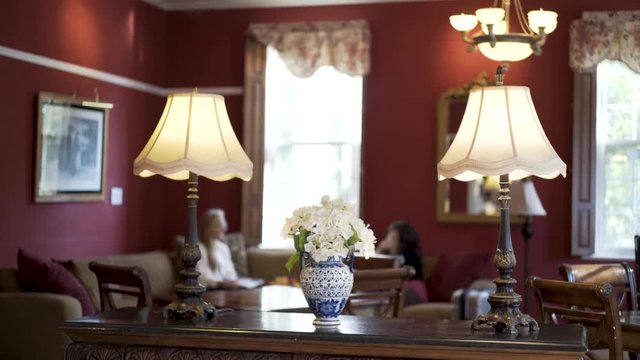 Flowers with table lamps in colonial red lounge with two women sitting and talking in background.