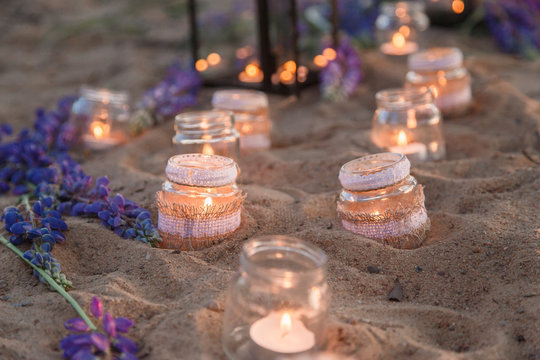 Beautiful decorated romantic place for a date with jars full of candles hanging on tree and standing on a sand. Copy Space