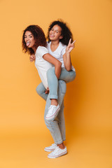 Full length portrait of cheery african girl carrying little sister