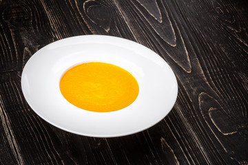 A bowl with pumpkin soup on a black wooden background