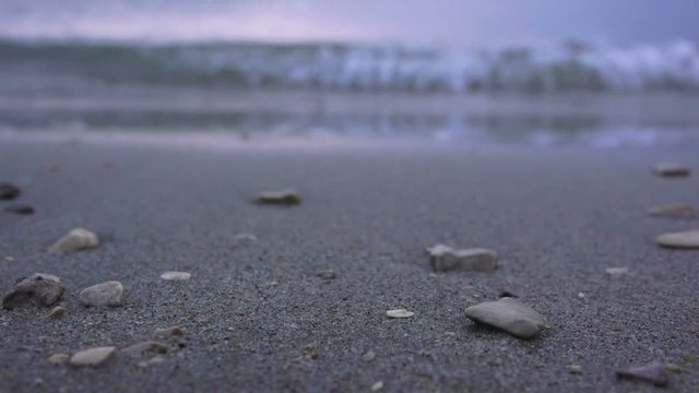Sea tidal wave at night splashing pebbles at sandy beach