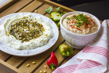 Middle Eastern dish - dense homemade labneh yoghurt with zatar in white dishes, on a wooden aged surface. Daylight.