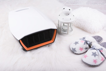 Fototapeta na wymiar Electric heater, pair of warm slippers and Christmas lantern on white furry carpet. Winter background.
