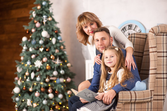 Family of mother, father and little child daughter near Christmas tree with presents, decorations and New Year or Christmas