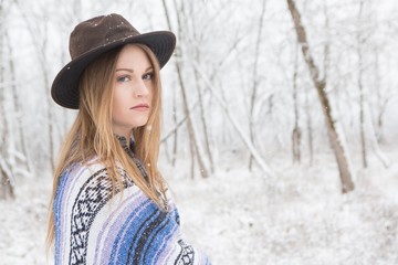 young woman in the snow wearing a bohemian style blanket and hat during a winter storm.