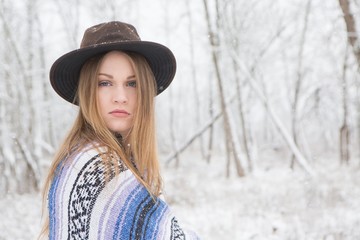 young woman in the snow wearing a bohemian style blanket and hat during a winter storm.