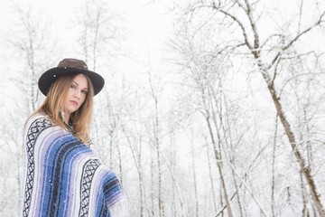 young woman in the snow wearing a bohemian style blanket and hat during a winter storm.