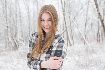 Young woman in black and white plaid shirt stading in a snow covered forrest.