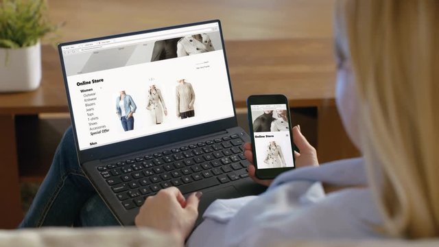 Woman Holds Smartphone and Has Laptop on Her Knees, Browses Online Store that Sales Fashionable Clothes.