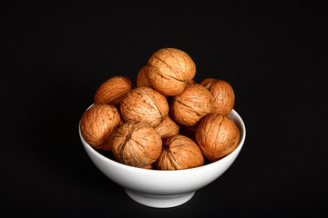 Ripe organic walnuts heaped in a white bowl and isolated on a black background  