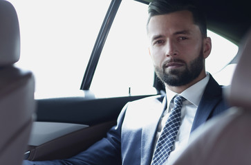 handsome bearded businessman sitting on back seat of car