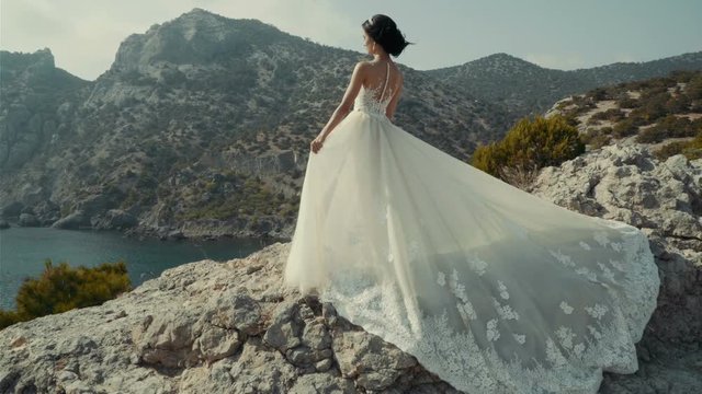 Romantic beautiful bride in white dress posing on terrace with sea and mountains in background