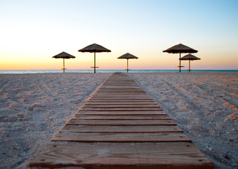 several a lot of big beach umbrellas made of straw and metal stand on the sea shore trail of wood path sand beach blue sea blue sky summer morning evening calm