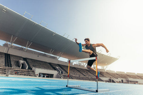 Fototapeta Athlete jumping over an hurdle on running track