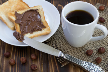 Bread with chocolate cream and coffee on the rustic wooden background