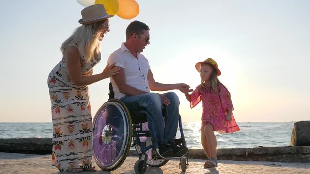 disabled husband on wheelchair with loved ones pregnant wife and kid in backlit resting near sea family on summer vacation