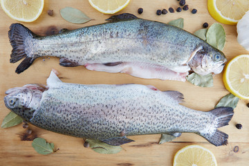 Horizontal shot of trout arranged on a wooden board surrounded by spices and lemon slices.  