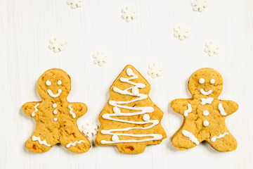 Gingerbread men friends at the Christmas tree on a white wooden table.